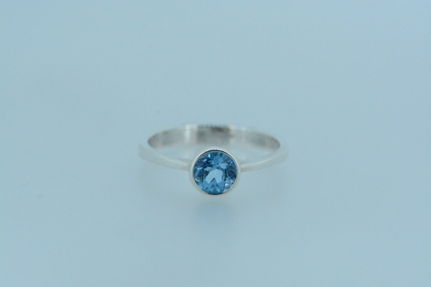 This light bright vibrant blue topaz stone in a round cut in a bezel setting set on a simple sterling silver band ring. An excellent choice with topaz - the birthstone for the month of November.