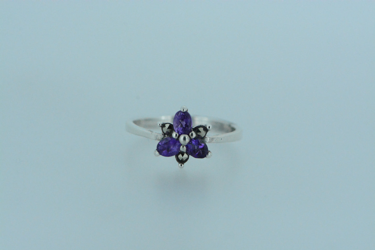 Inspired by nature, this flower ring has three purple amethyst stone petals and three smaller marcasite petals. This dainty ring is both feminine and floral with the birthstone for the month of February.