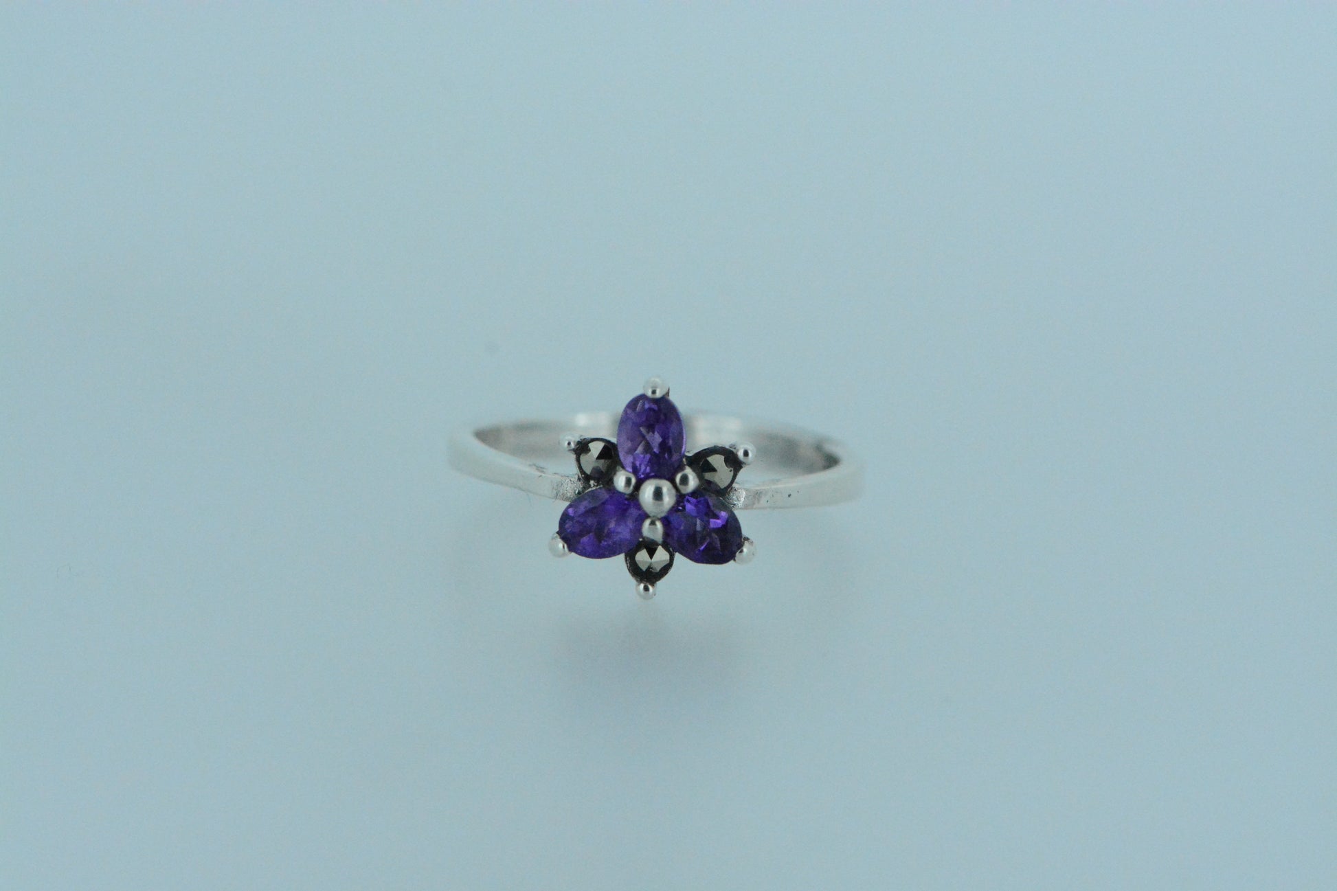 Inspired by nature, this flower ring has three purple amethyst stone petals and three smaller marcasite petals. This dainty ring is both feminine and floral with the birthstone for the month of February.