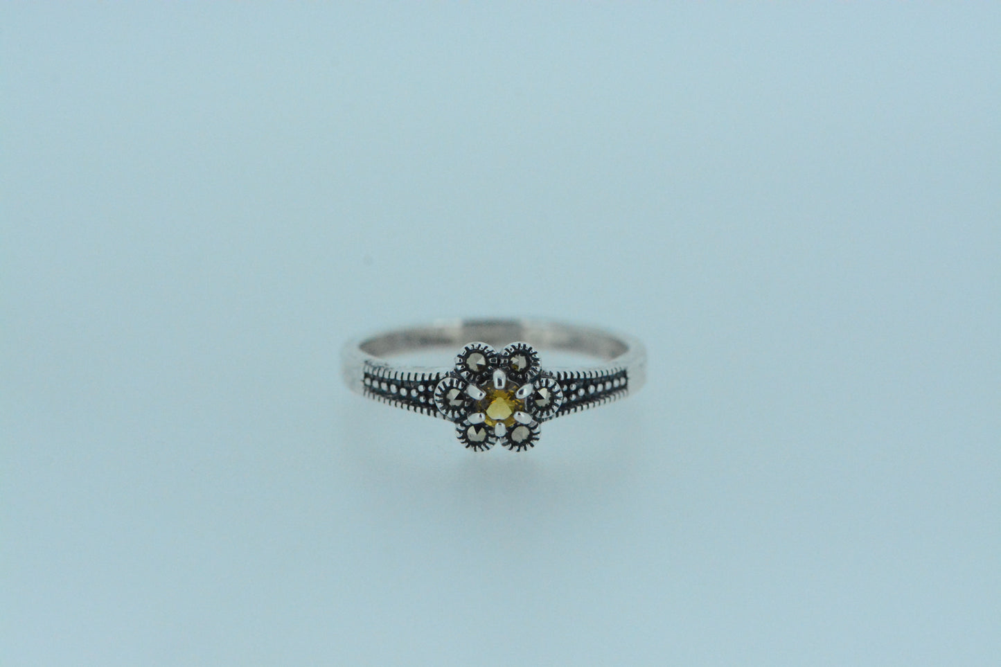 This claw set vibrant yellow citrine gem is at centre of the flower with six marcasite petals. Small beads set against darkened silver line the front of the in sterling silver band.