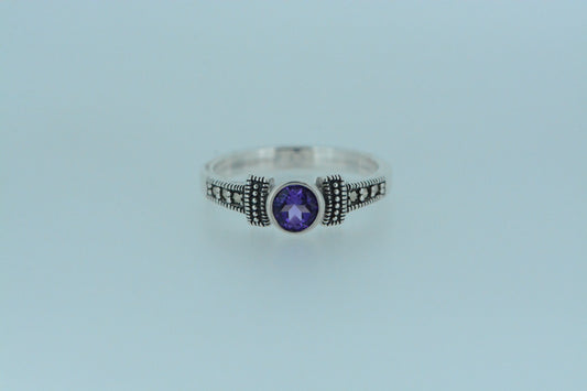 This round cut amethyst stone in a bezel setting is framed by two dashes with lines of polished silver balls on darkened silver. Round marcasite stones also adorn the front of the band.