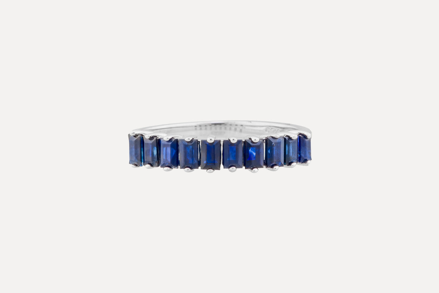 A half circle of blue baguette cut sapphires set onto a sterling silver ring with rhodium plating for a dazzling finish. Creating a simple yet sophisticated and timeless look.