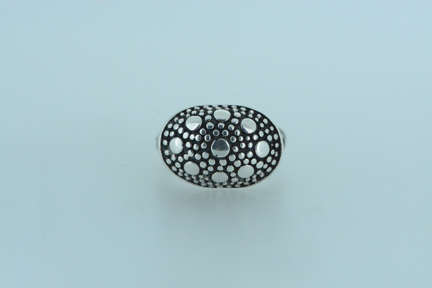 A bold interplay of texture and contrast, this hand made sterling silver ring features an oval shaped dome with an array of polished silver circles in various sizes, set on a black oxidised surface.