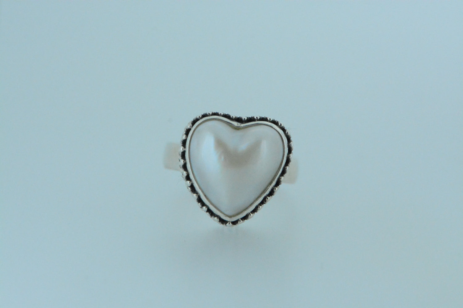 This sterling silver ring showcases a heart shaped pearl surrounded by a beaded &amp; filigree designs set onto a simple band ring. Symbolic of love, this large pearl makes a statement.