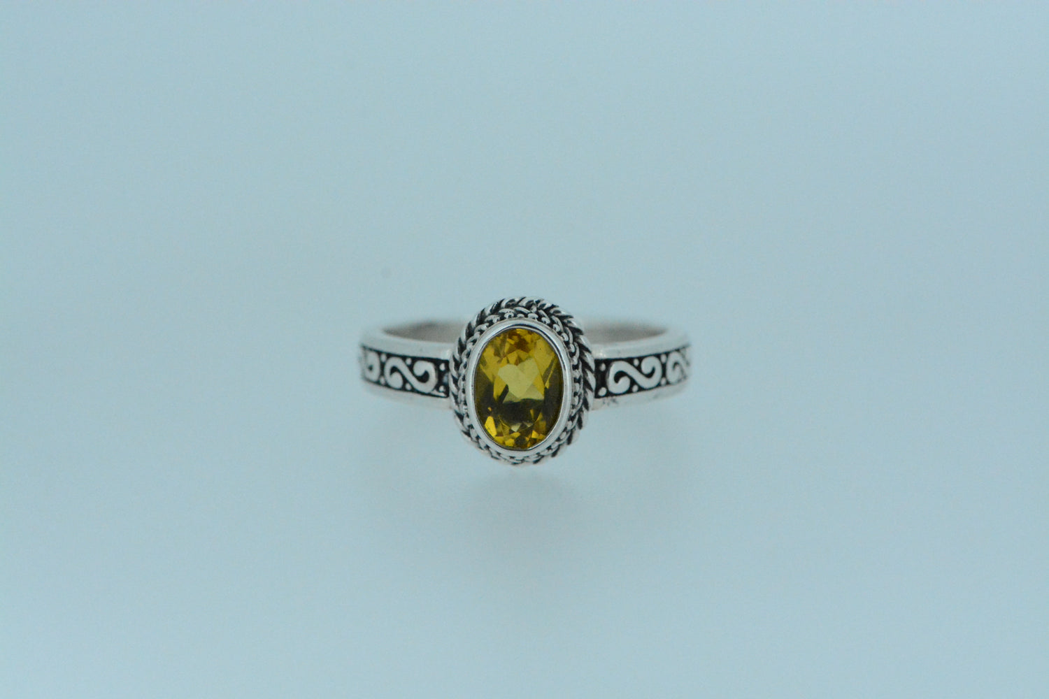 This ring with an oval citrine at the centre has a halo of woven silver around it. The band sides are sculpted with S shapes on darkened silver. A charming ring with the birthstone of November.