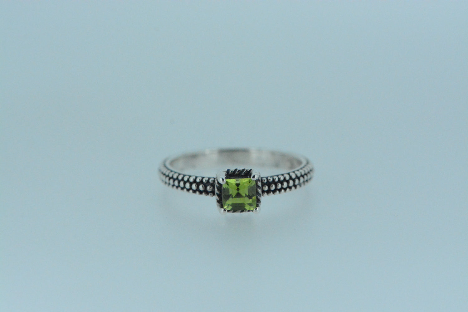This sterling silver ring with polished silver beads that encircle the band on darkened silver showcases a beautiful green square peridot stone, making an excellent choice with the birthstone for the month of August.