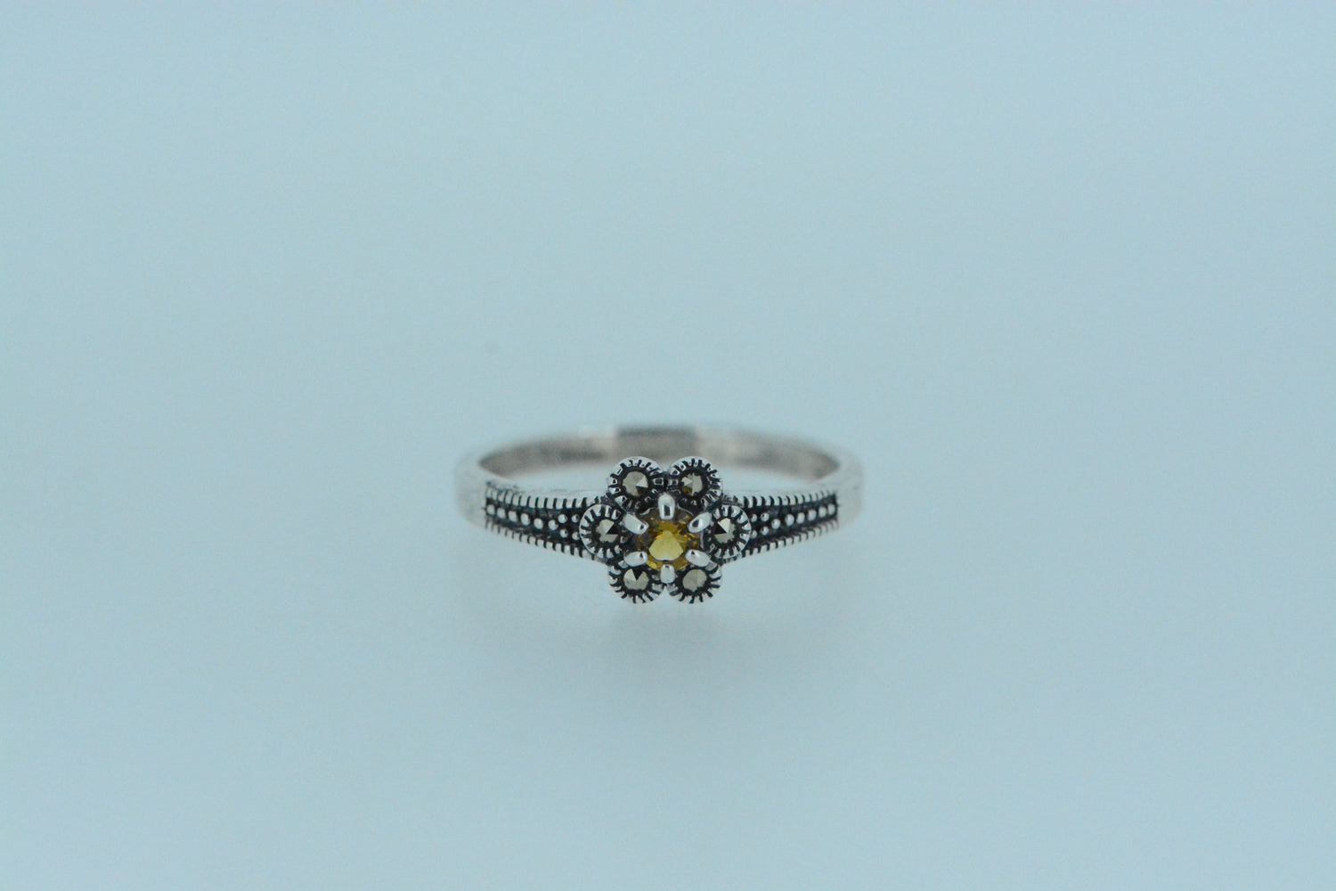 This claw set vibrant yellow citrine gem is at centre of the flower with six marcasite petals. Small beads set against darkened silver line the front of the in sterling silver band.