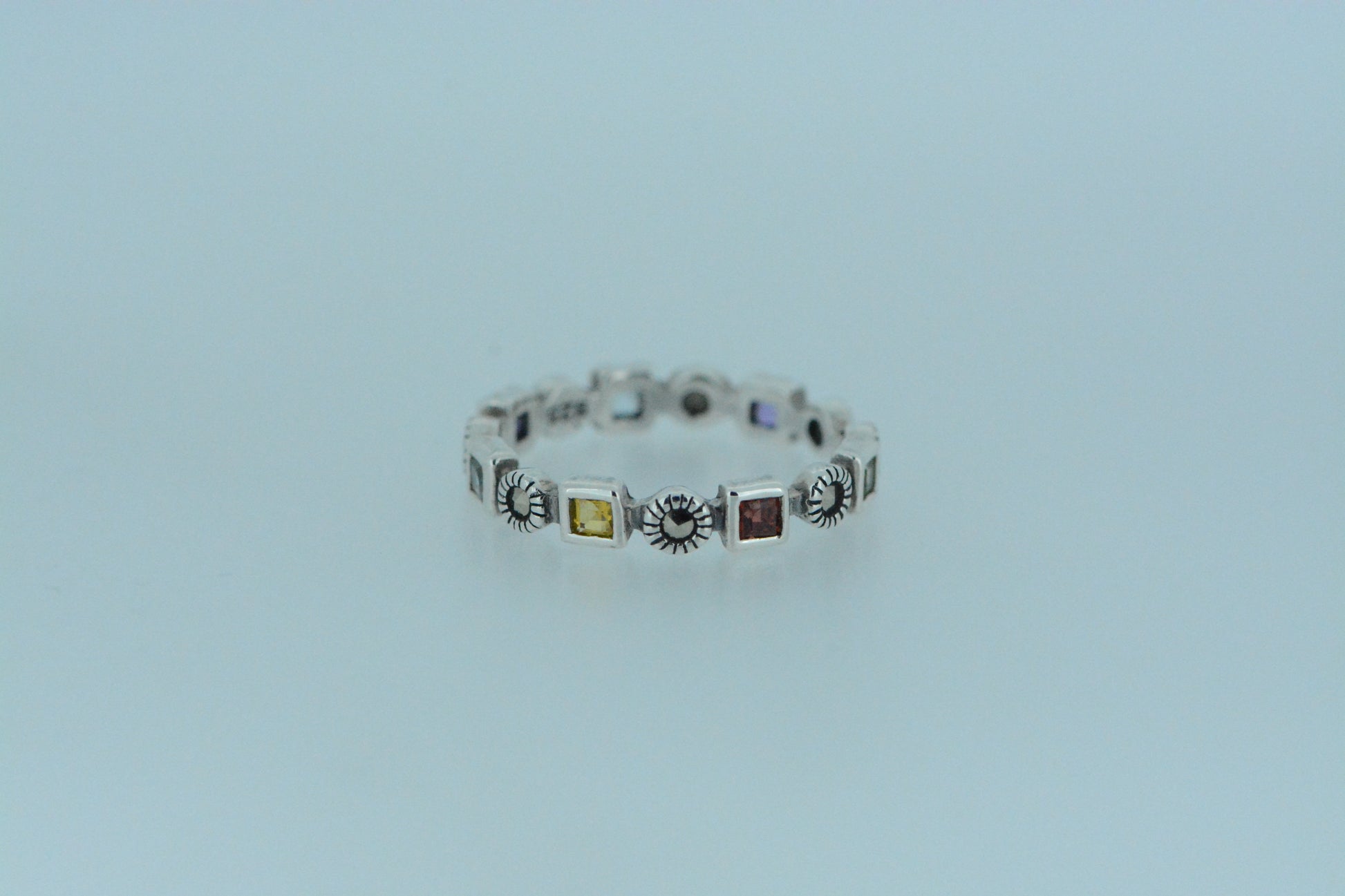A silver ring with multicolored gemstones set in a row on a white background